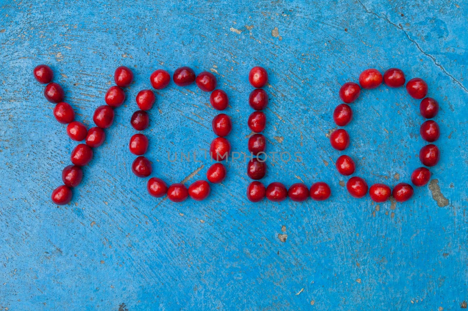 Cherries arranged to form the word YOLO on textured blue background