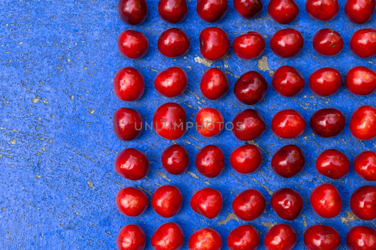 Square arrangement of ripe cherries on blue textrured background, cherry pattern
