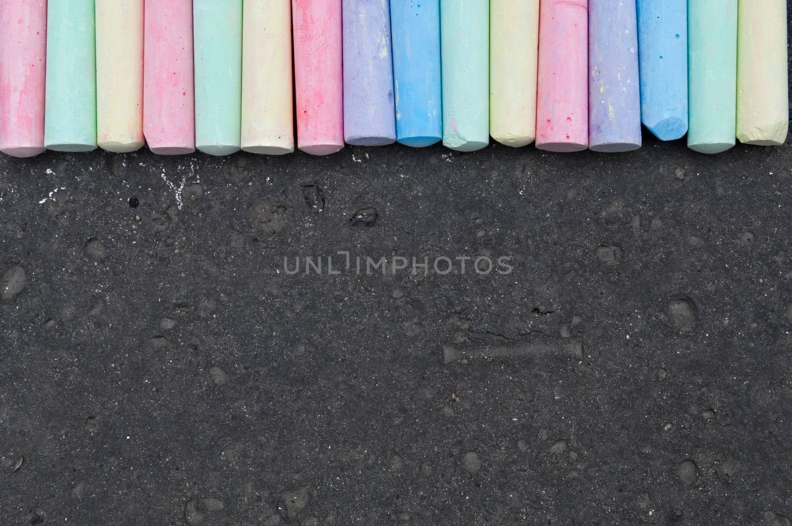 Colorful pastel sidewalk chalk on dark asphalt background. Top view