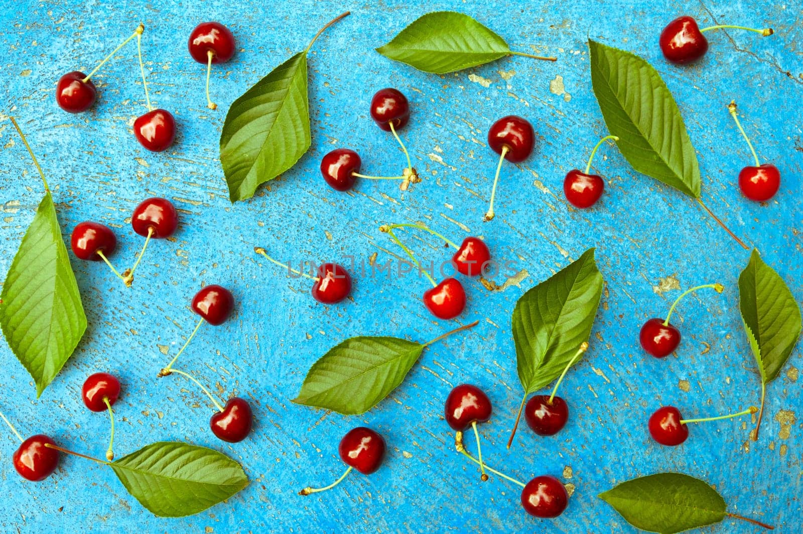 Cherry, cherries with cherry leaves on textured light blue background, top view