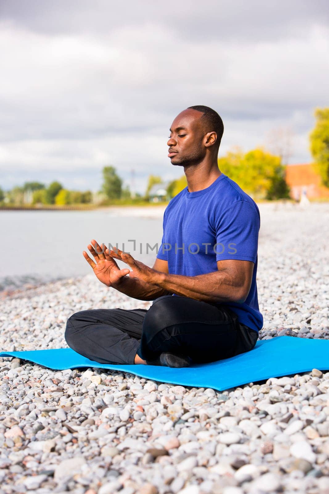 young black man wearing athletic wear sitting on the beach exercising yoga