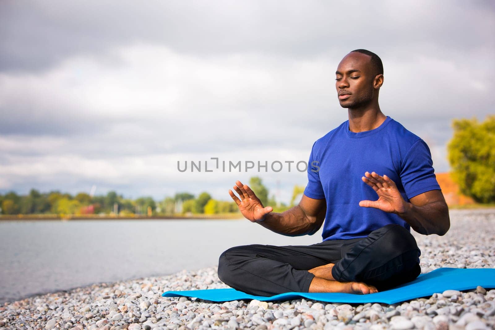 young black man wearing athletic wear sitting on the beach exercising yoga