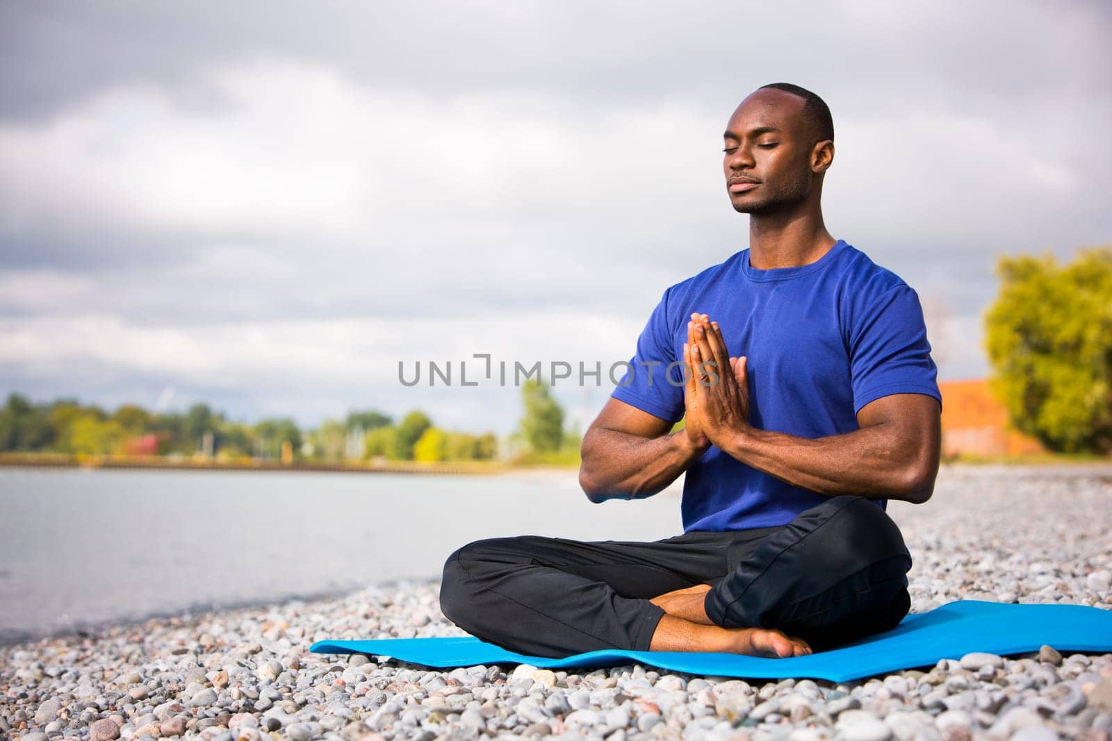 young black man wearing athletic wear sitting on the beach exercising yoga