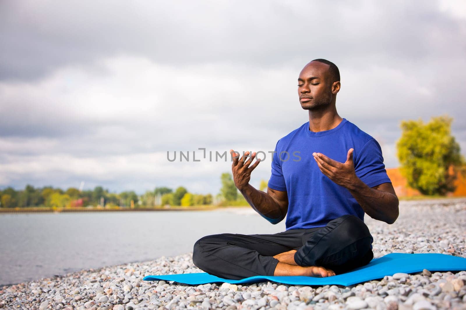 young black man wearing athletic wear sitting on the beach exercising yoga