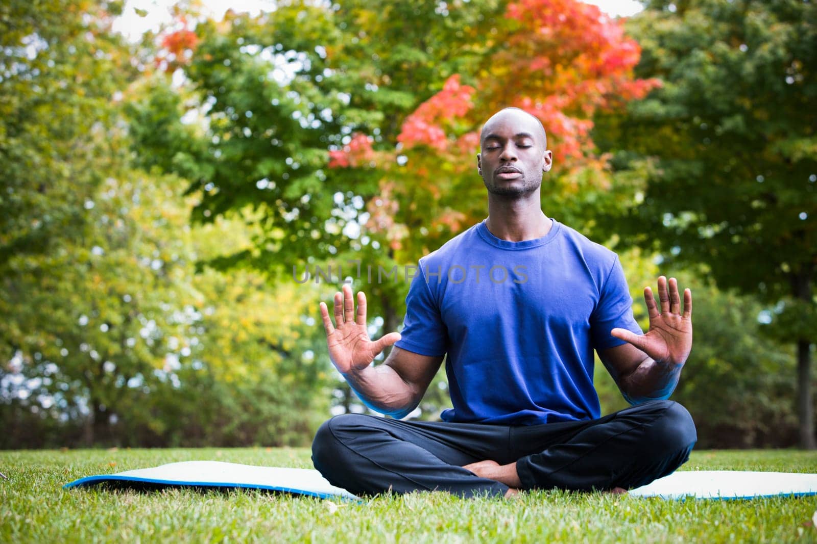young black man wearing athletic wear sitting in the park exercising yoga