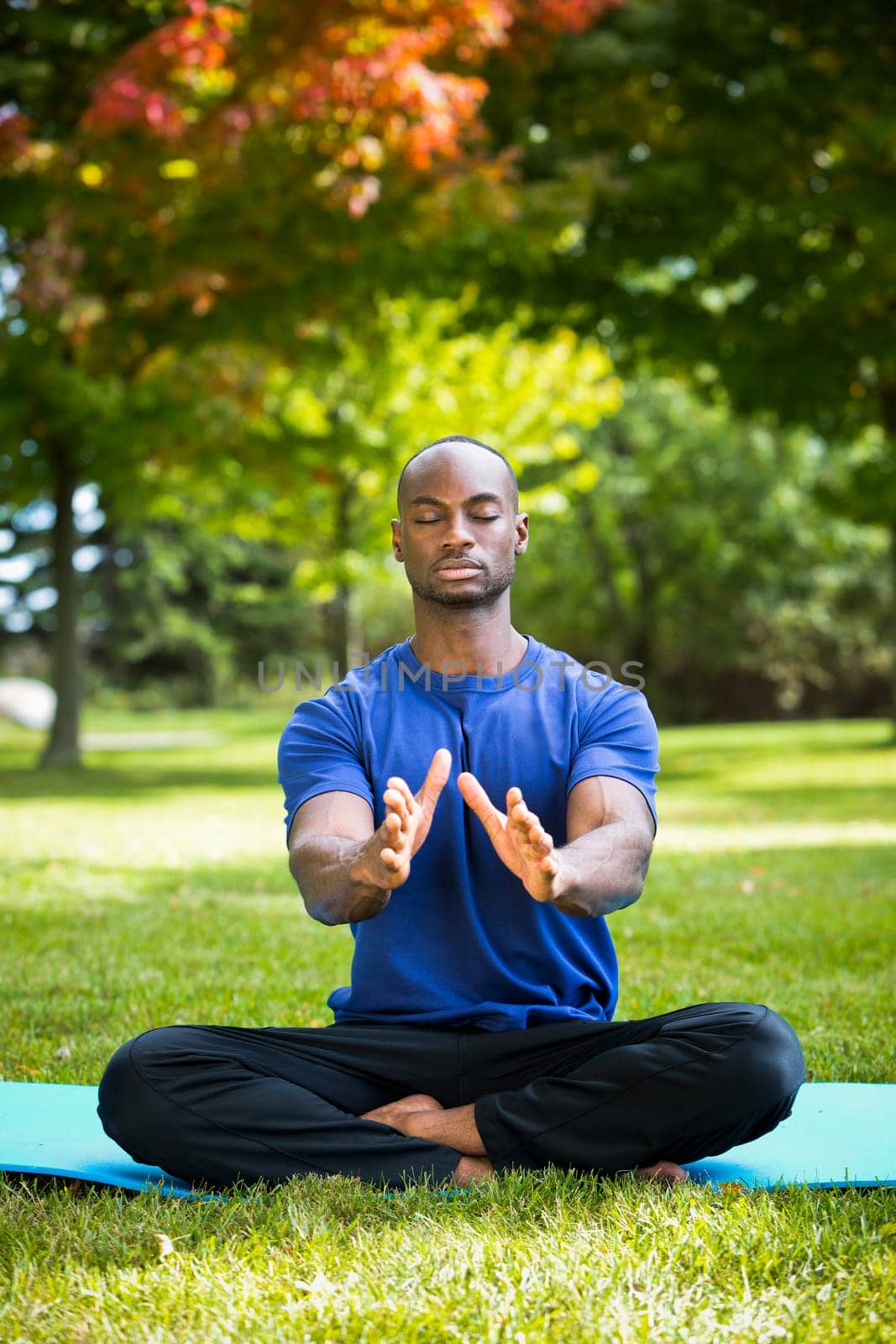 young black man wearing athletic wear sitting in the park exercising yoga