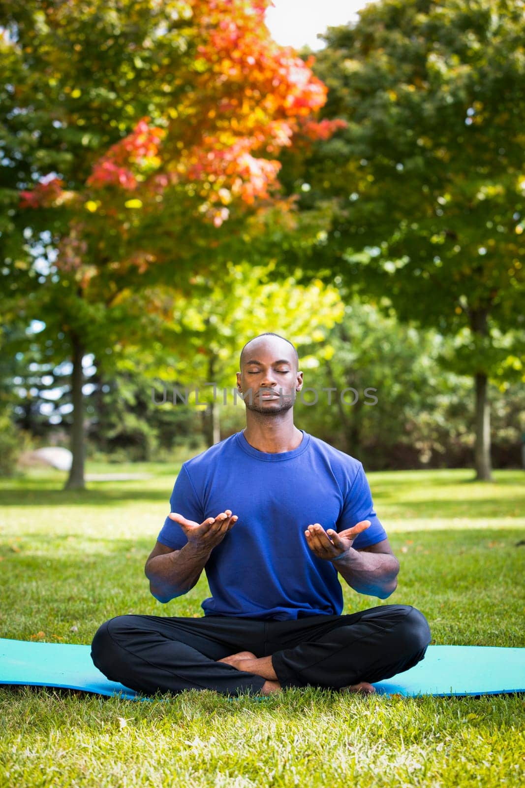 young black man wearing athletic wear sitting in the park exercising yoga