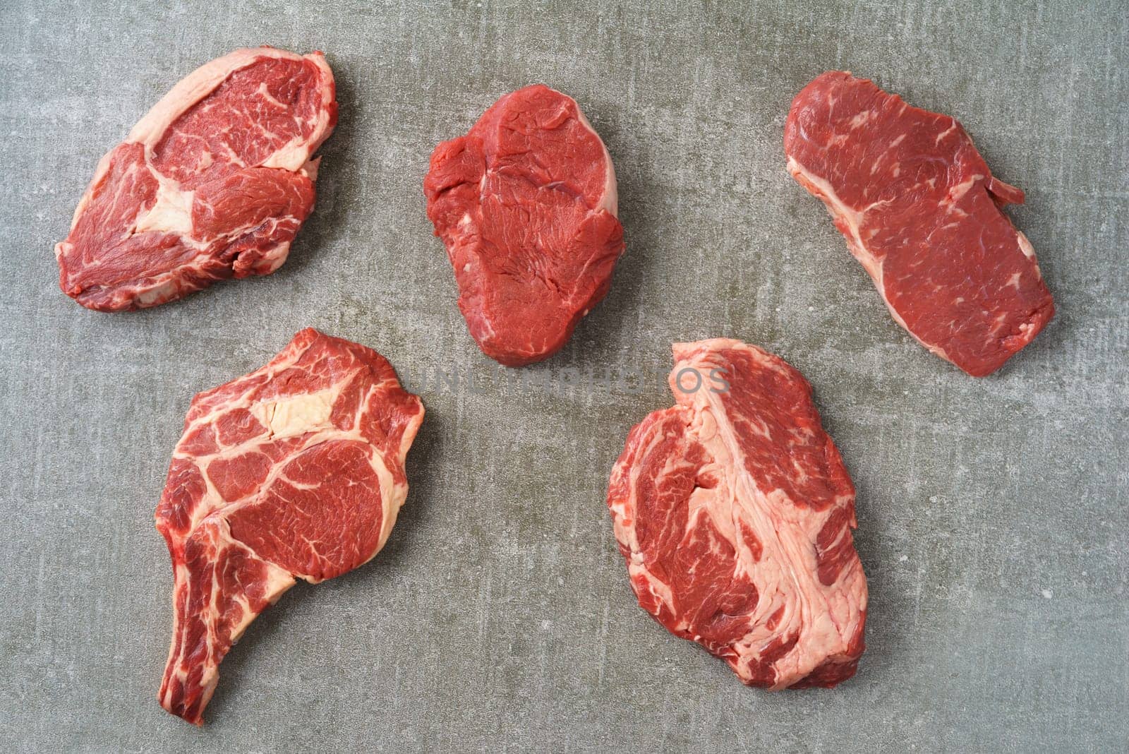 Variety of different beef steaks on grey stone