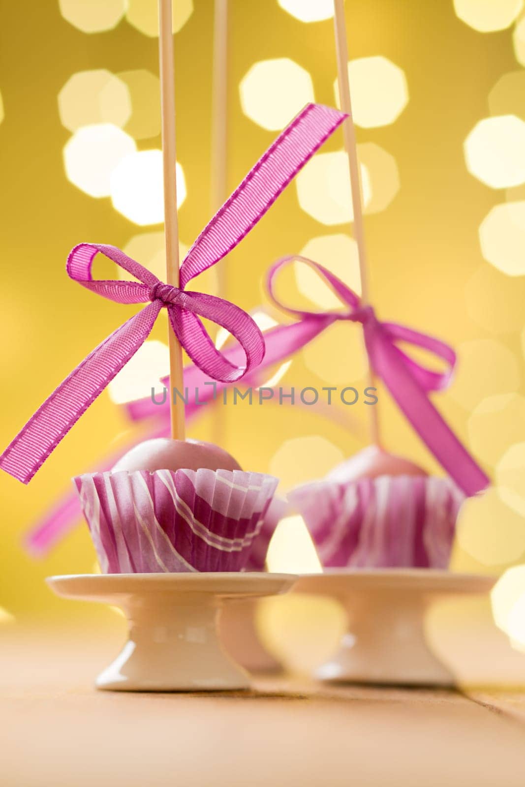 Pink Christmas cake pops sticking upside down in miniature cupcake liners. Very shallow depth of field with Christmas lights in the background