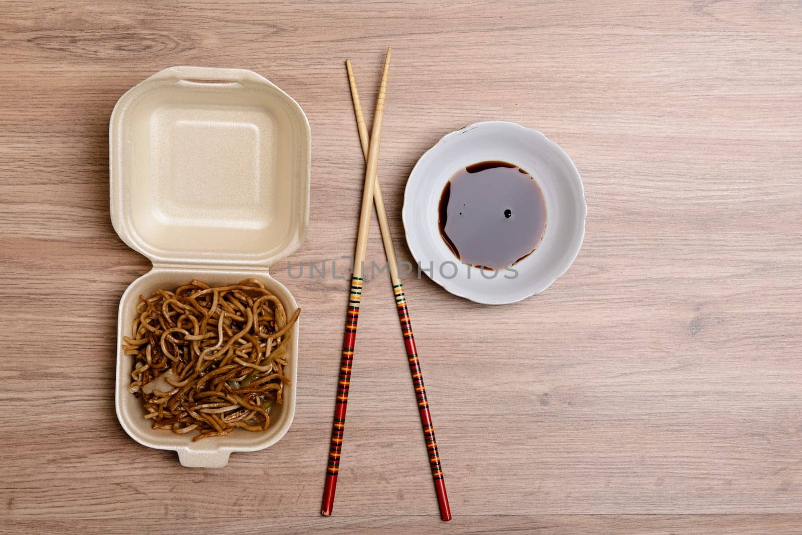chinese nooles in box with chopsticks and soy sauce on wooden ground from above