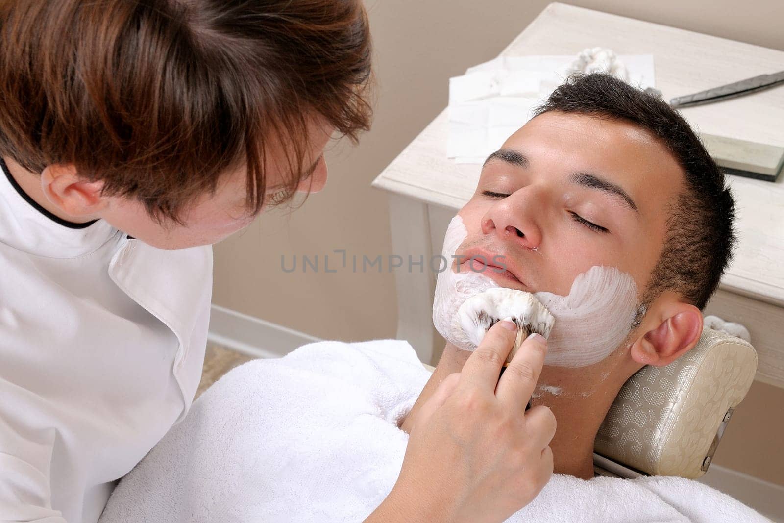 Shaving at the barber of a young boy in retro style with razor and shaving soap