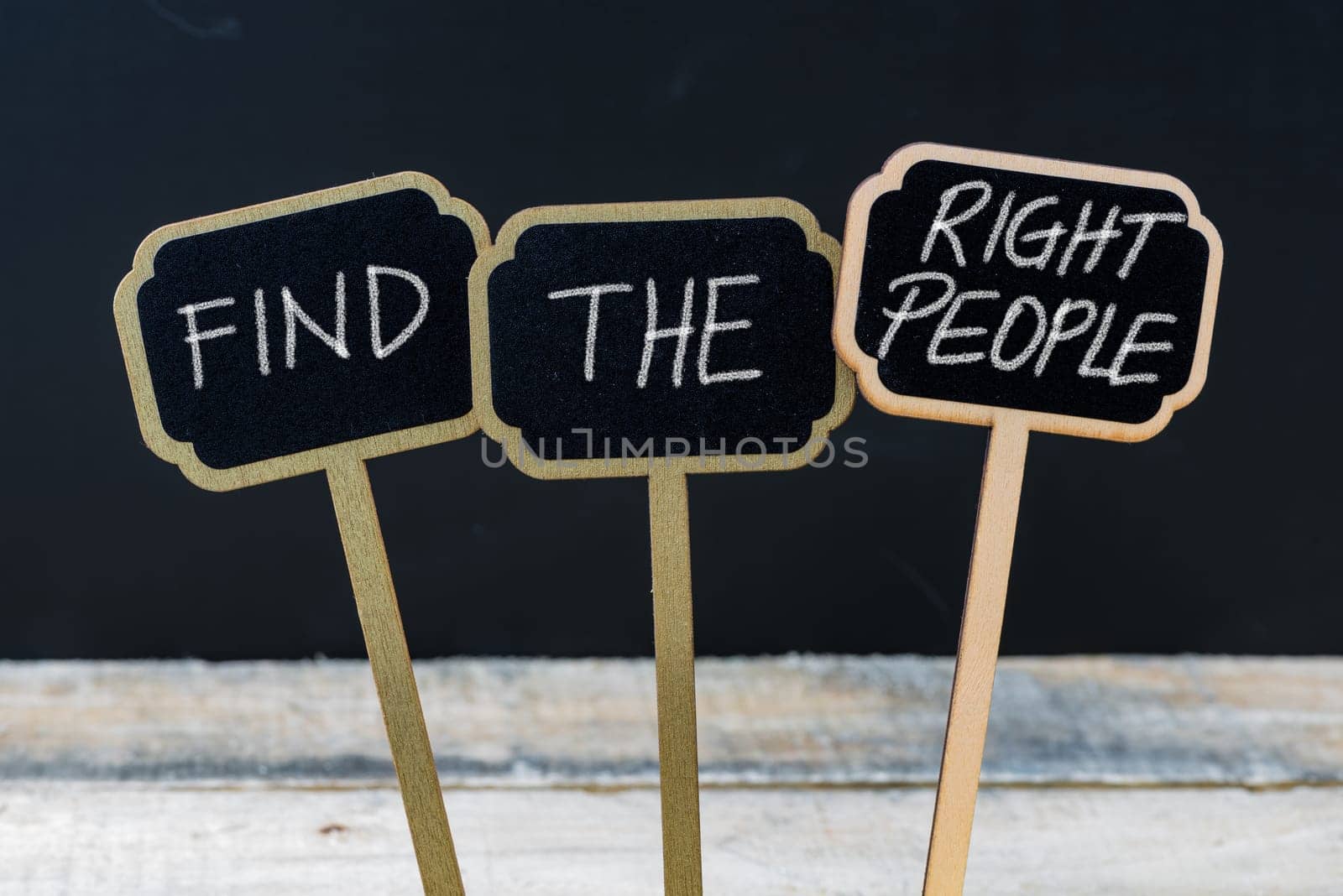 Business message FIND THE RIGHT PEOPLE written with chalk on wooden mini blackboard labels, defocused chalkboard and wood table in background