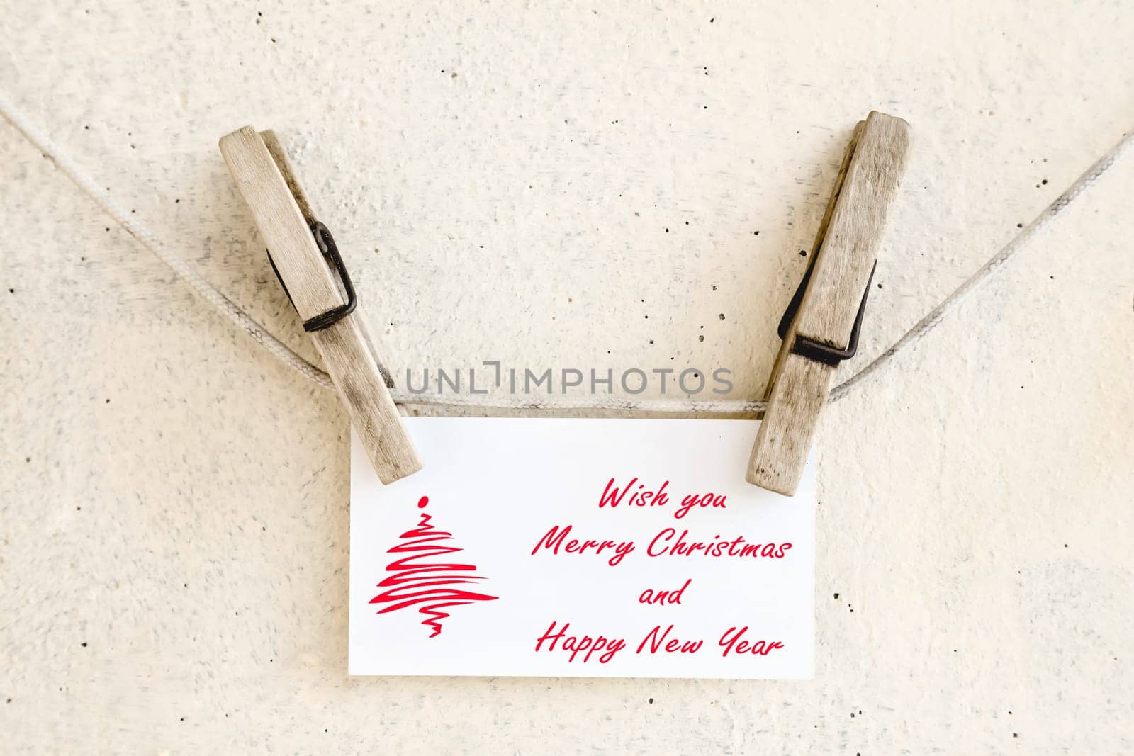 Clothespins holding on clothesline or rope holding christmas greeting card on plaster background
