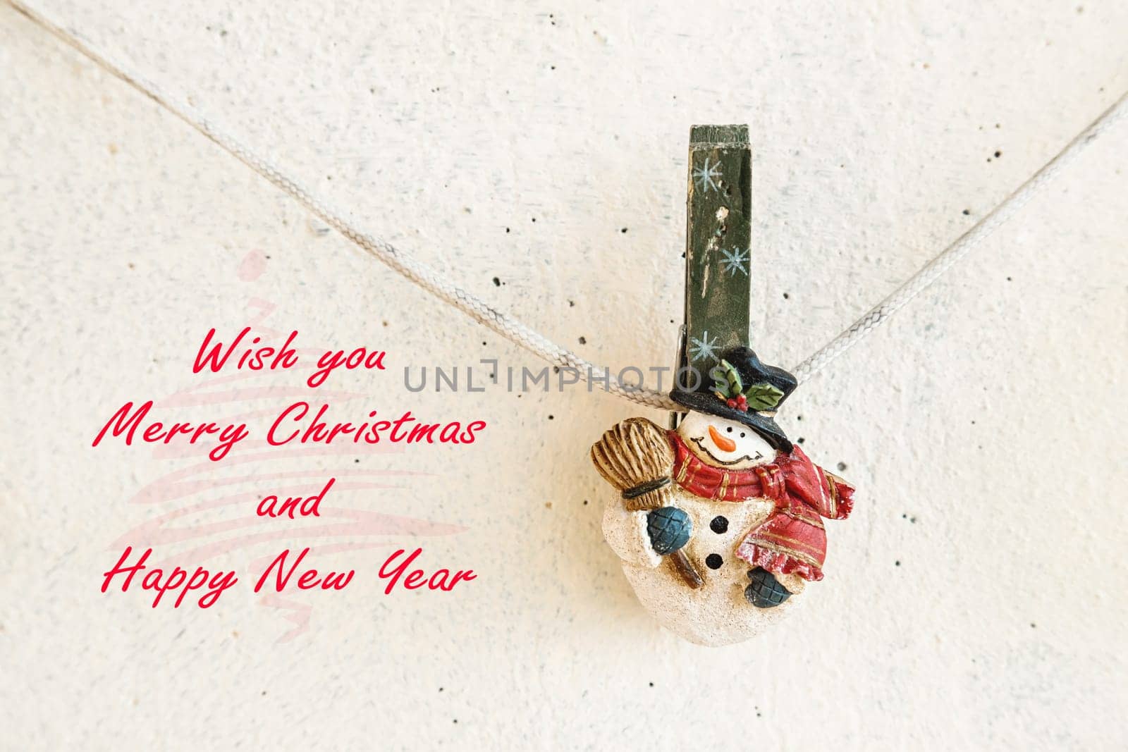 Christmas greeting card with snowman clothespin hanging on clothesline or rope on plaster background