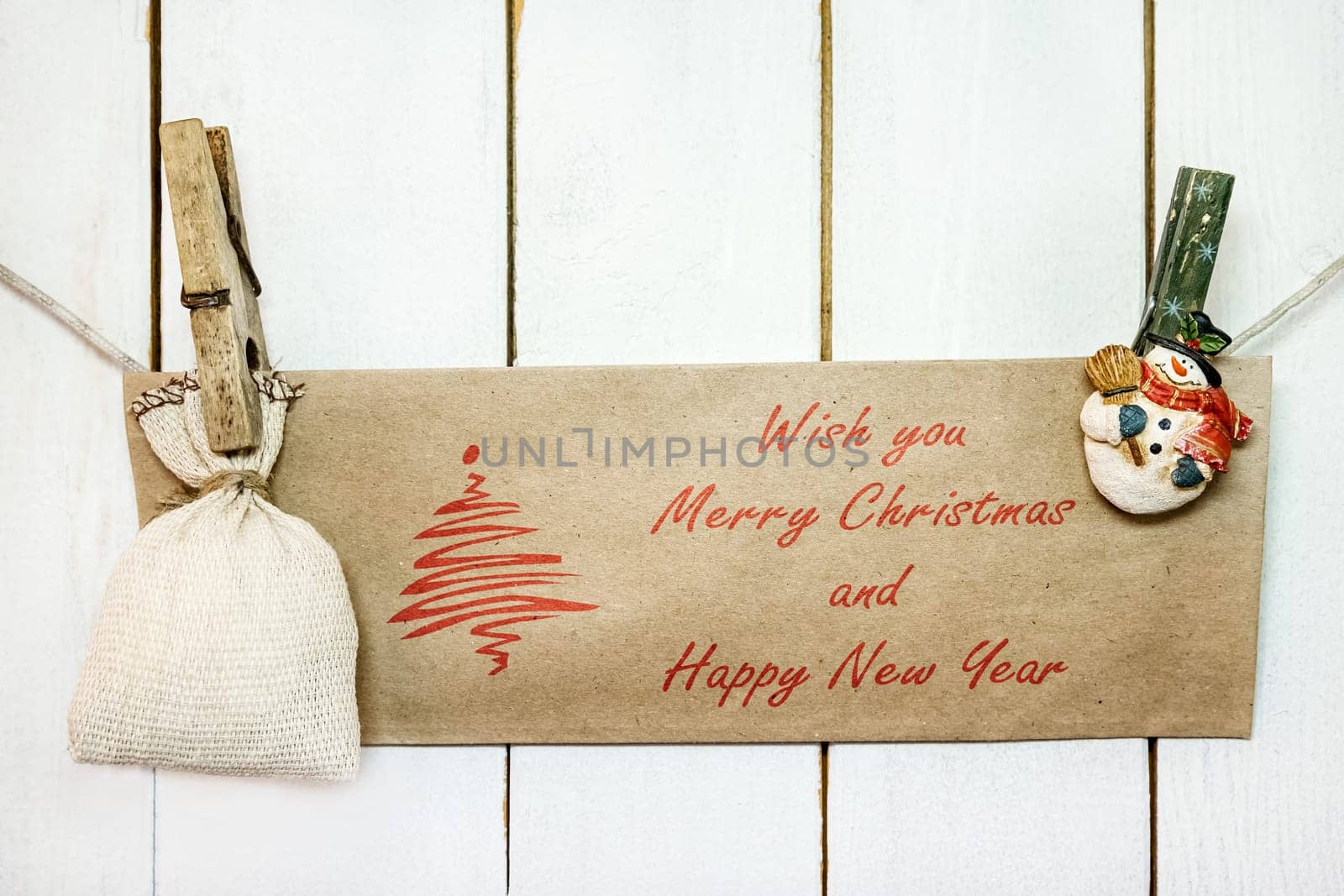 Christmas snowman clothespins hanging on clothesline or rope and holding brown Christmas greeting card and sack on wood background