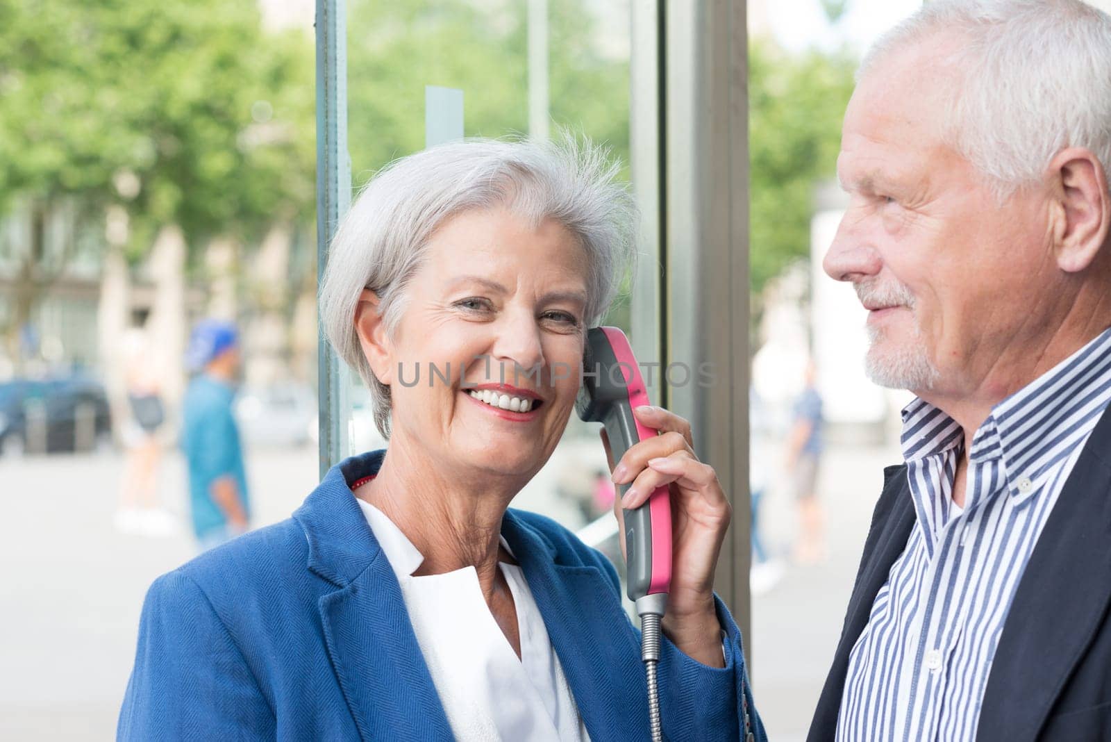 Two seniors stand at a public telephone booth and make phone calls
