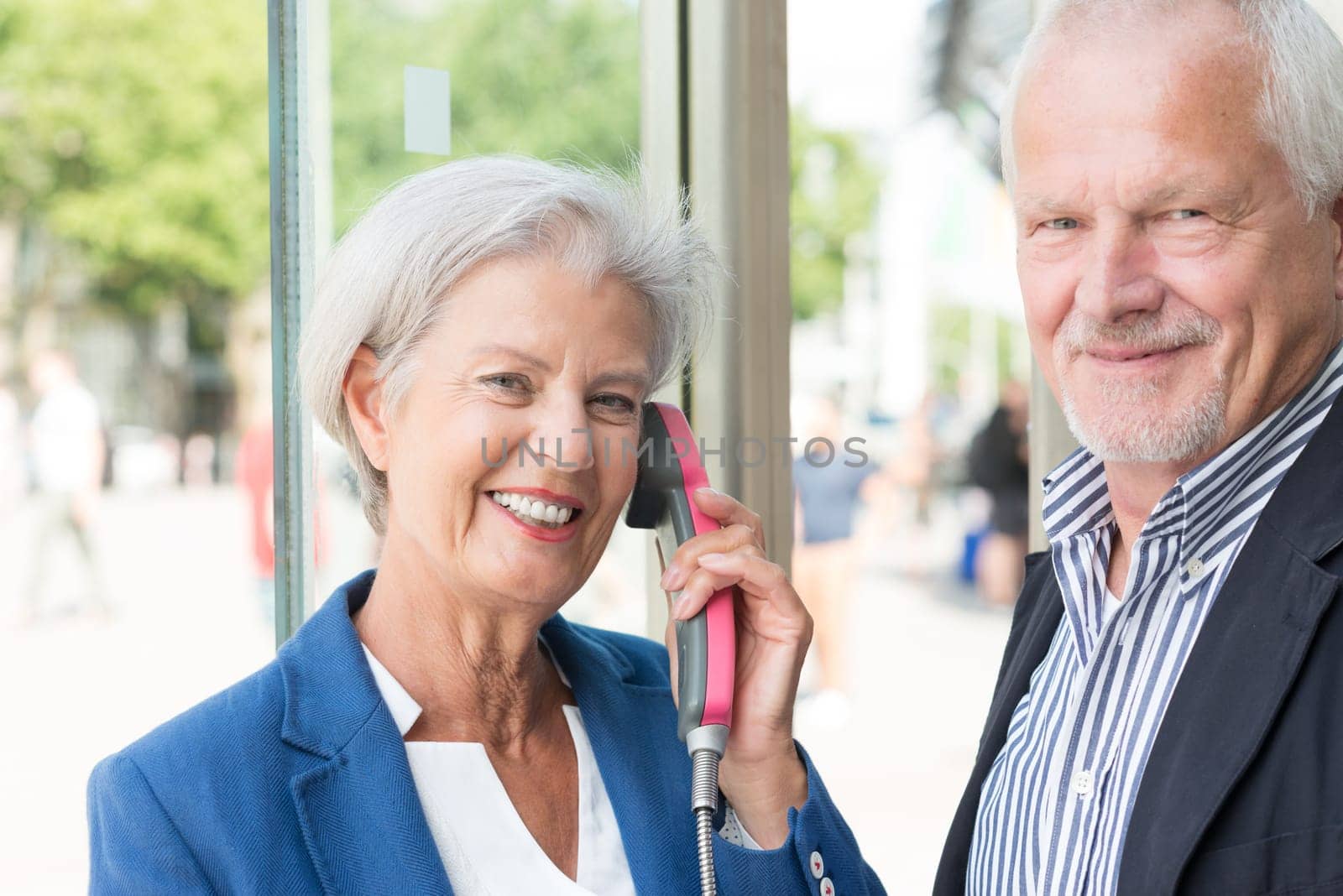 Two seniors stand at a public telephone booth and make phone calls