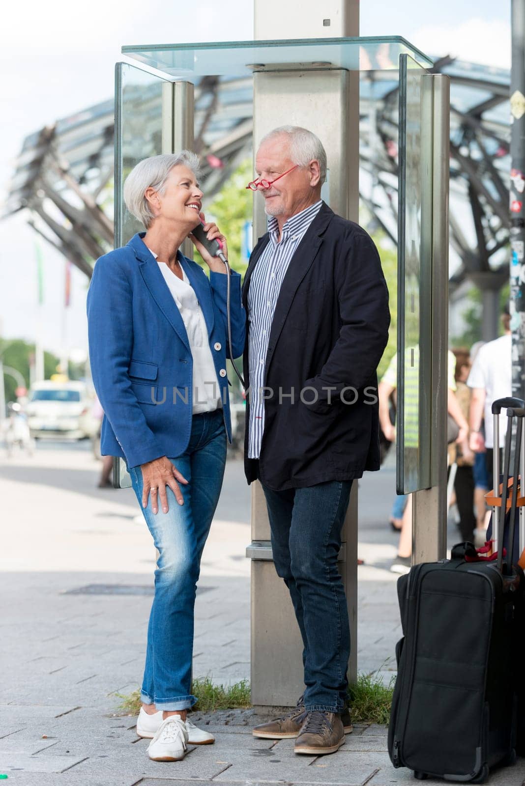 Two seniors stand at a public telephone booth and make phone calls