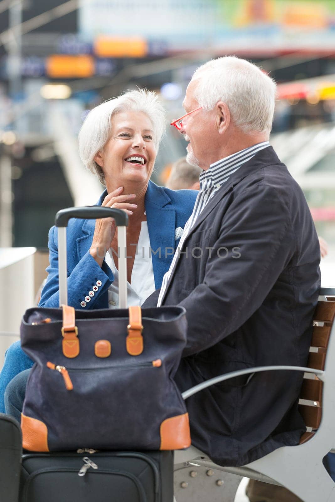 Two laughing seniors on a bench in the train station