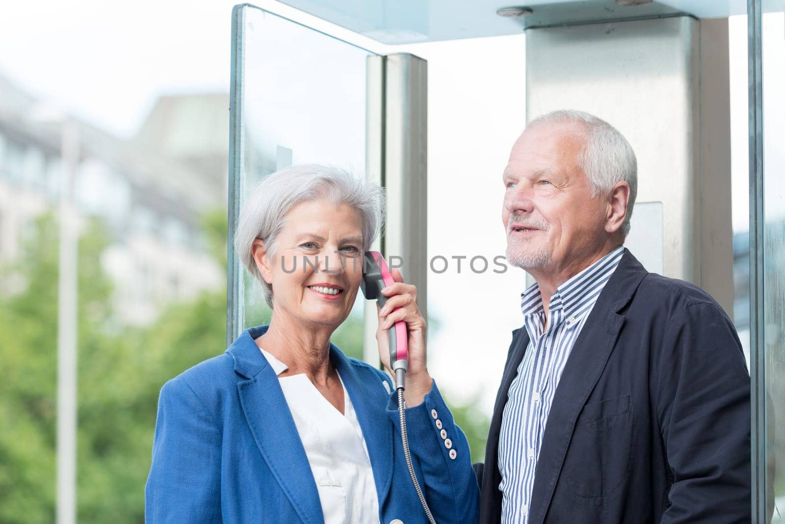 Two seniors stand at a public telephone booth and make phone calls