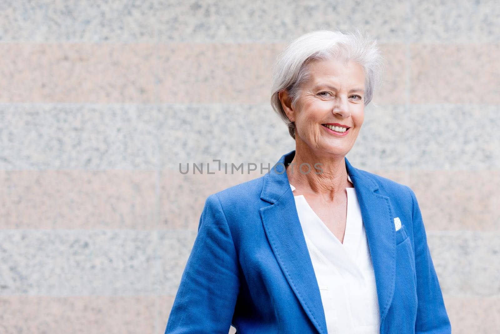 Smiling senior citizen with gray hair in front of a wall