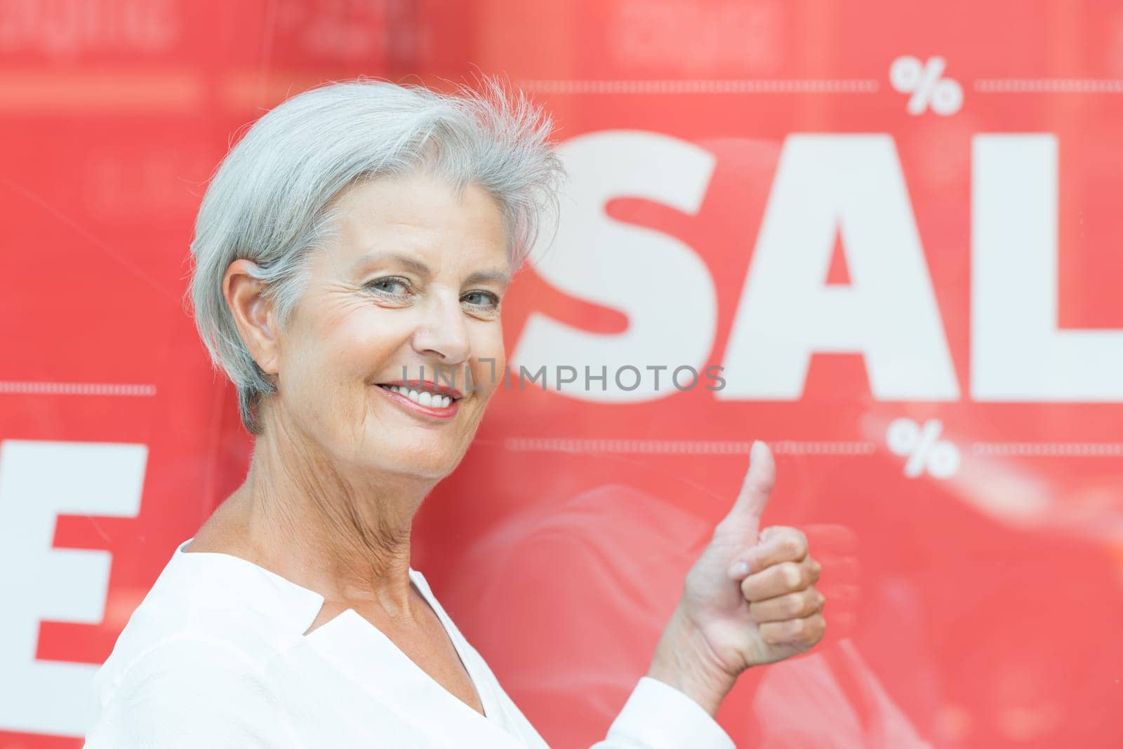 Smiling senior citizen in front of a shop window with a sale sign