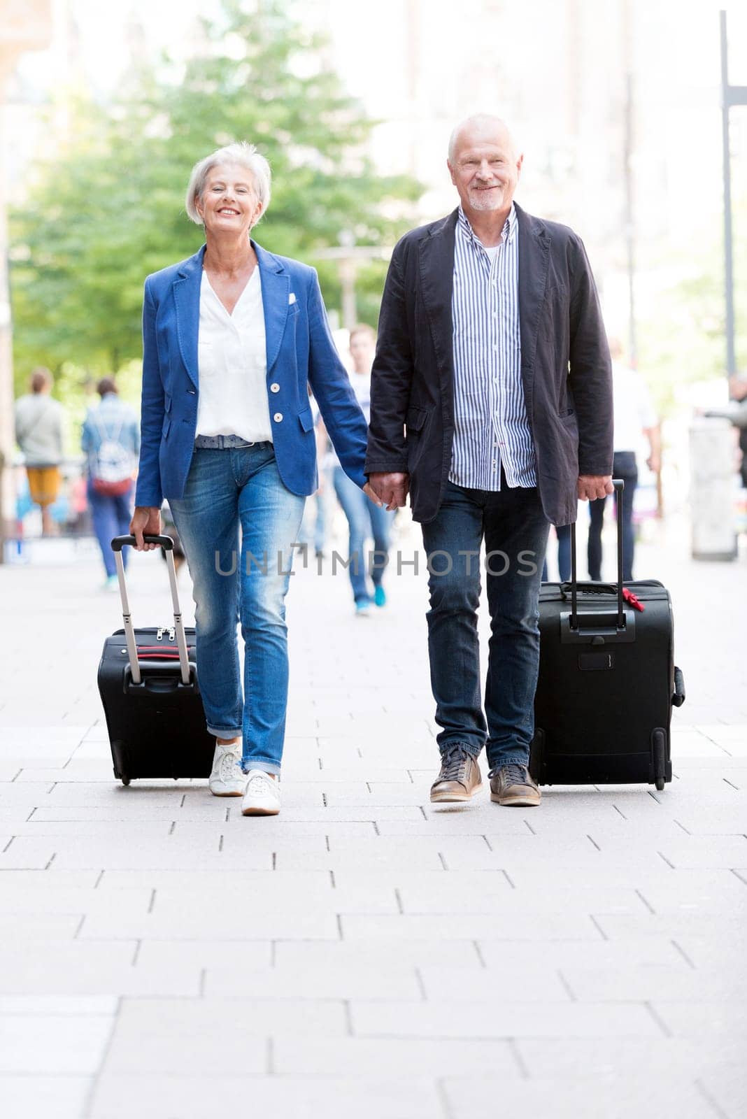 Two seniors with suitcases on a sidewalk