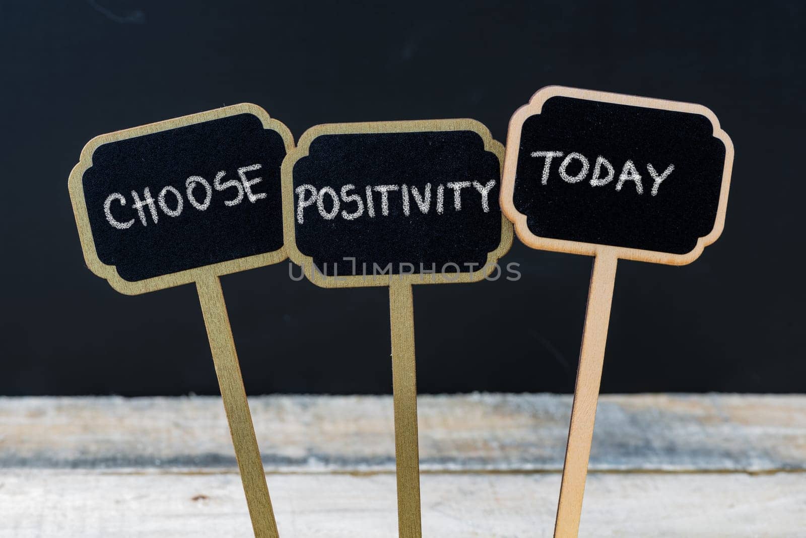 Business message CHOOSE POSITIVITY TODAY written with chalk on wooden mini blackboard labels, defocused chalkboard and wood table in background