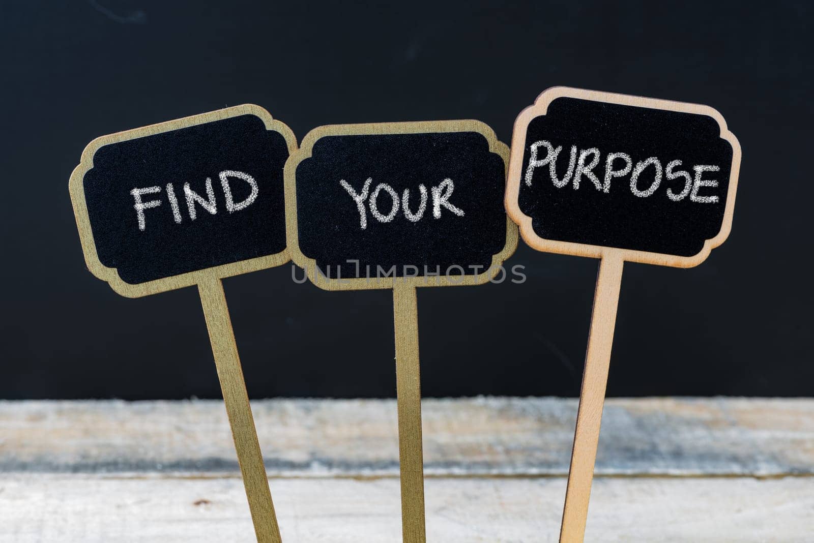 Business message FIND YOUR PURPOSE written with chalk on wooden mini blackboard labels, defocused chalkboard and wood table in background
