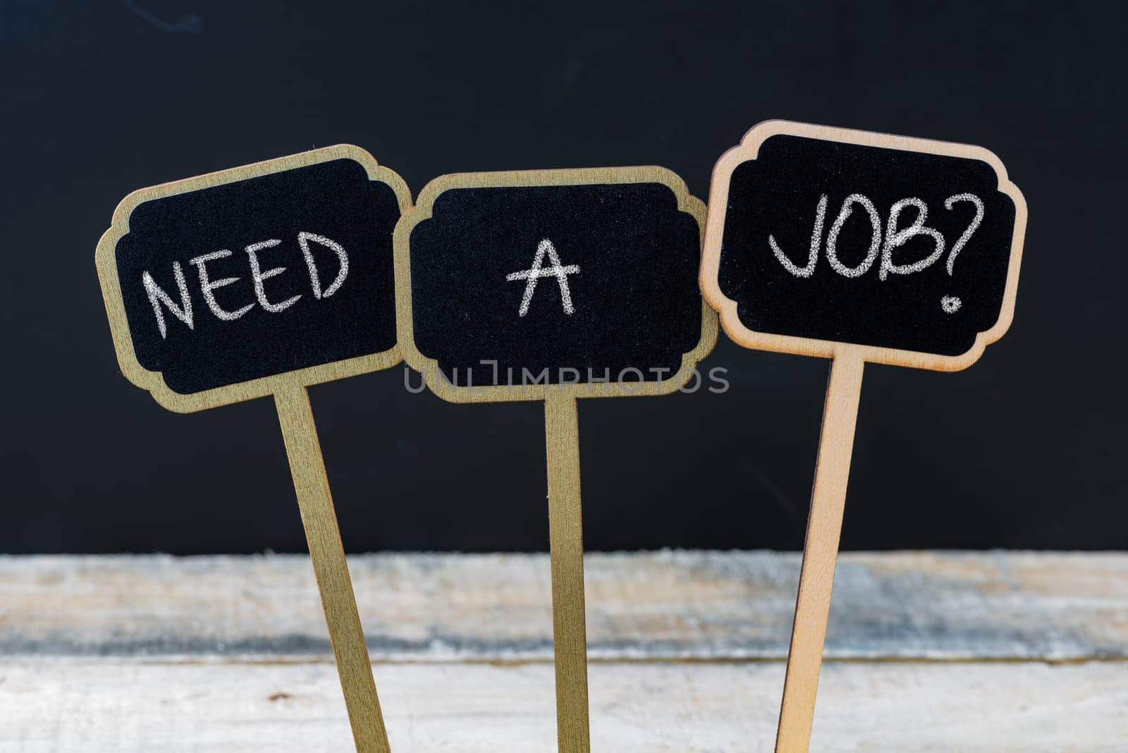 Business message NEED A JOB ? written with chalk on wooden mini blackboard labels, defocused chalkboard and wood table in background