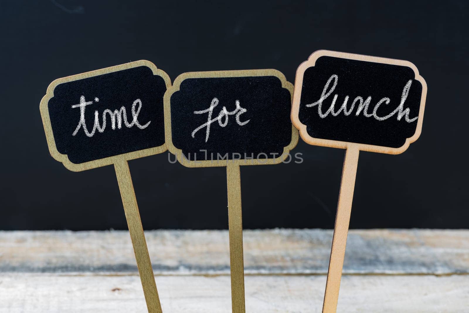 Business message TIME FOR LUNCH written with chalk on wooden mini blackboard labels, defocused chalkboard and wood table in background
