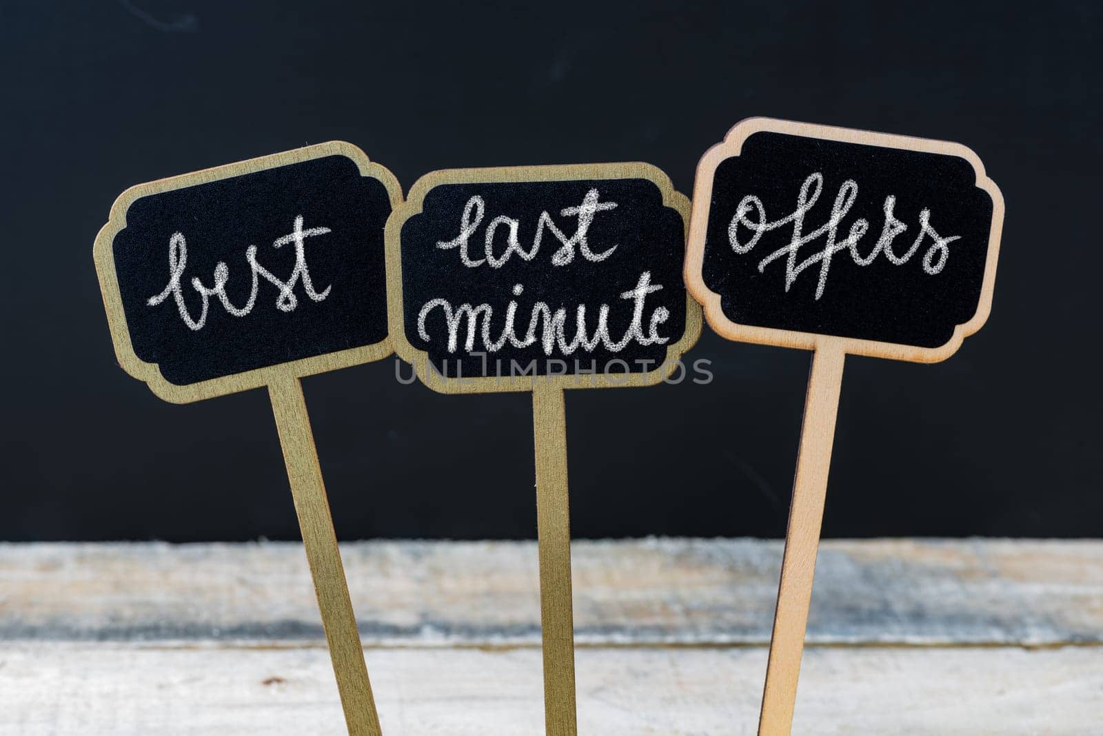 Business message BEST LAST MINUTE OFFERS written with chalk on wooden mini blackboard labels, defocused chalkboard and wood table in background