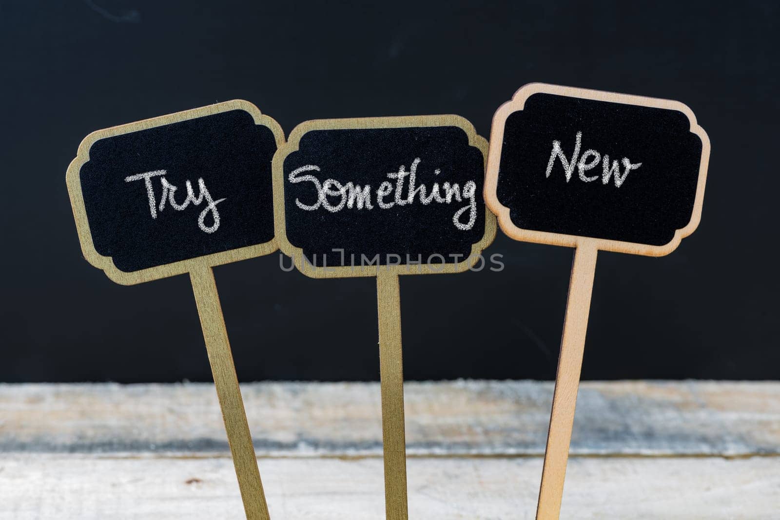 Business message TRY SOMETHING NEW written with chalk on wooden mini blackboard labels, defocused chalkboard and wood table in background