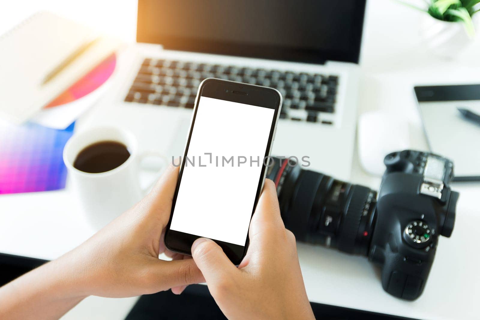 creative photogeapher holding phone white screen on workspace table, phone blank screen for adjustment mobile app