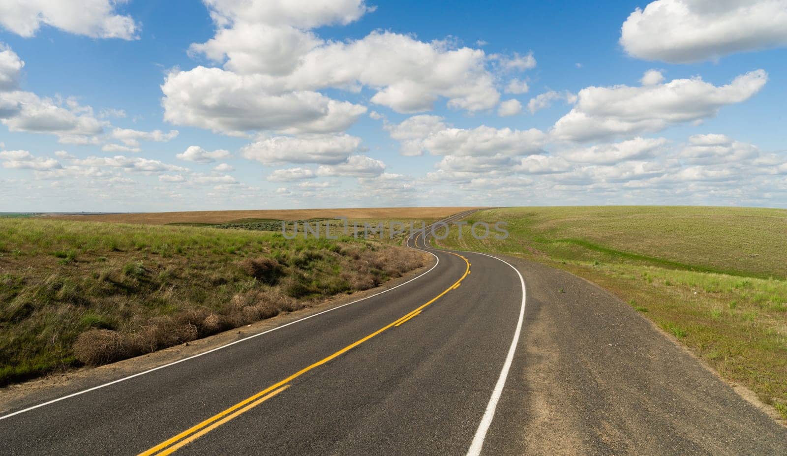 A central Washington State road winds out into the distance below fluffy blue clouds