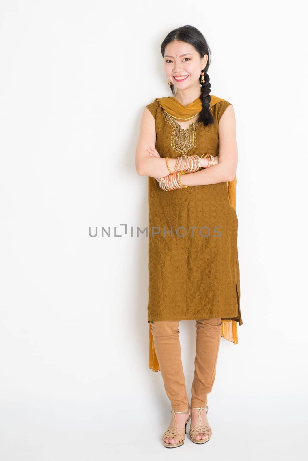 Portrait of young mixed race Indian Chinese female in traditional punjabi dress smiling, full length standing on plain white background.