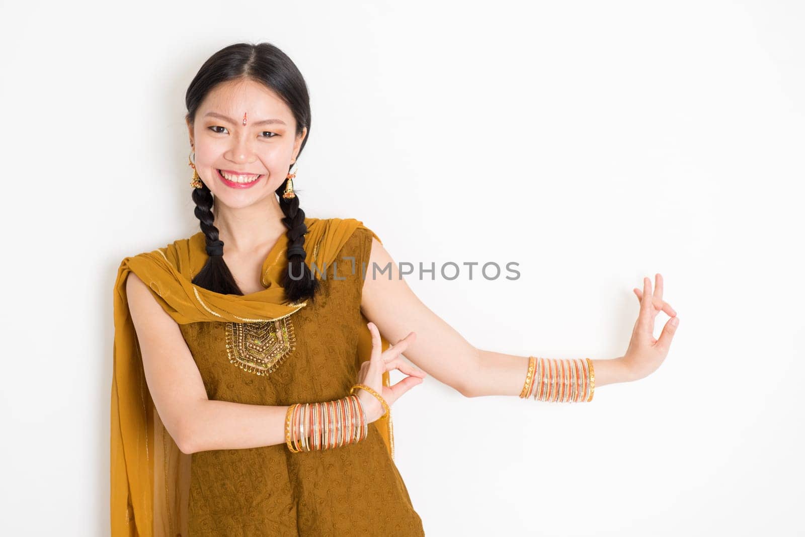 Portrait of young mixed race Indian Chinese girl dancer in traditional punjabi dress with dancing pose, standing on plain white background.
