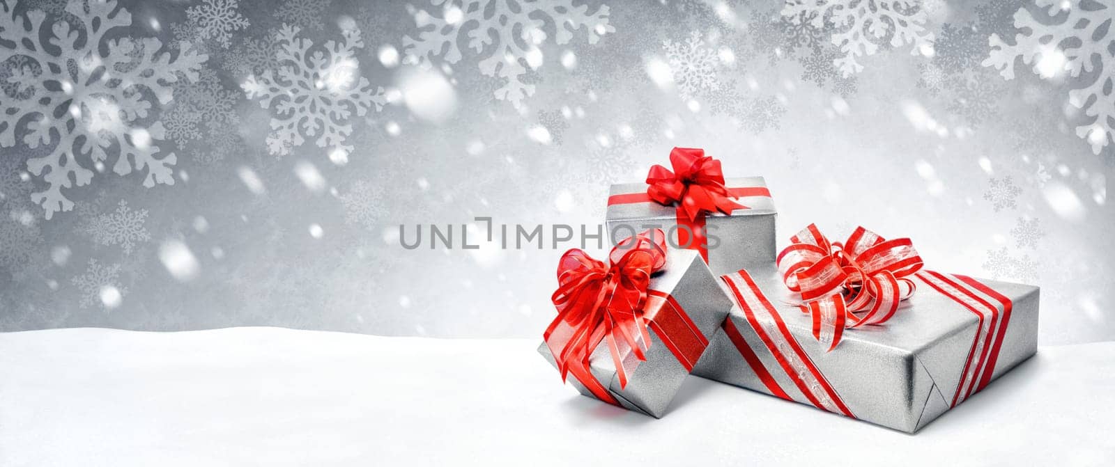 Silver Christmas or birthday gift boxes with red bows in snow,with symbolic snow background,panorama format