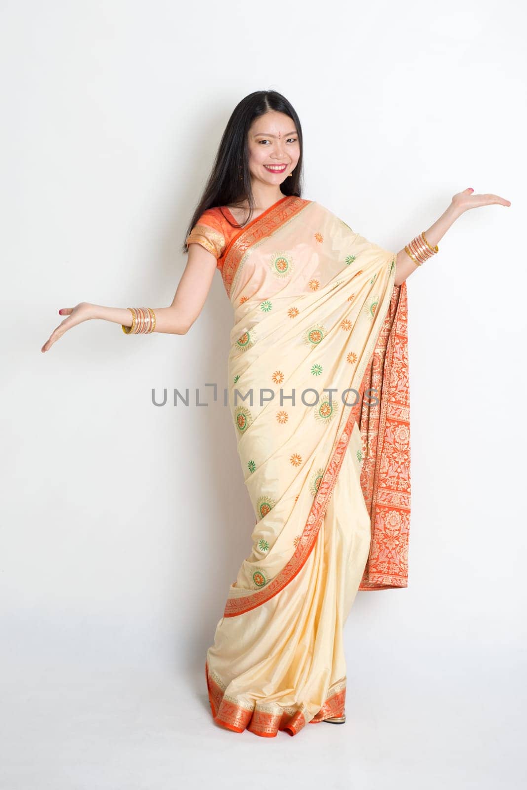 Portrait of young mixed race Indian Chinese woman in traditional sari dress dancing, on plain background.