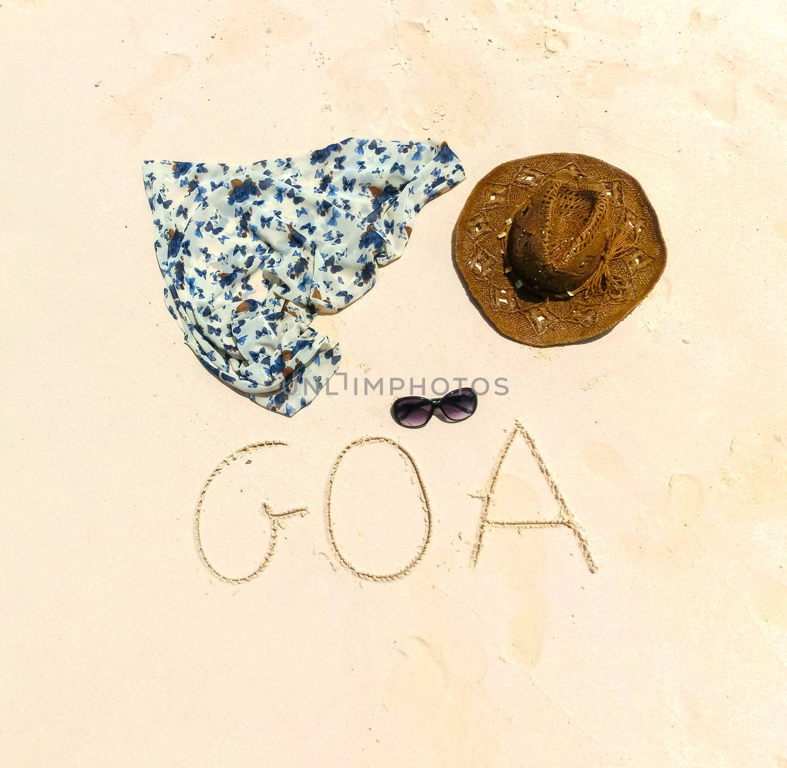 The straw hat, mask, sun glasses and dress on a tropical beach and inscription on sand Goa .