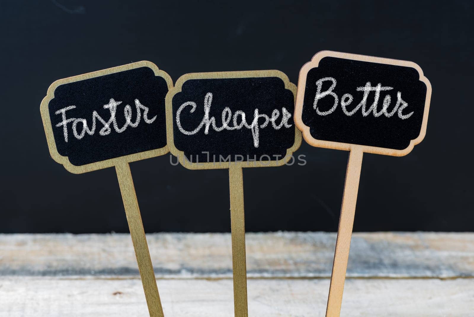 Business message Faster, Cheaper, Better written with chalk on wooden mini blackboard labels, defocused chalkboard and wood table in background