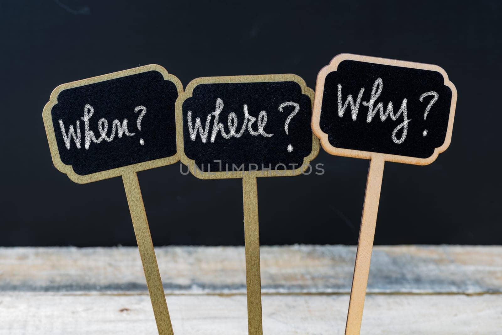 Business message When ? Where ? Why ? written with chalk on wooden mini blackboard labels, defocused chalkboard and wood table in background