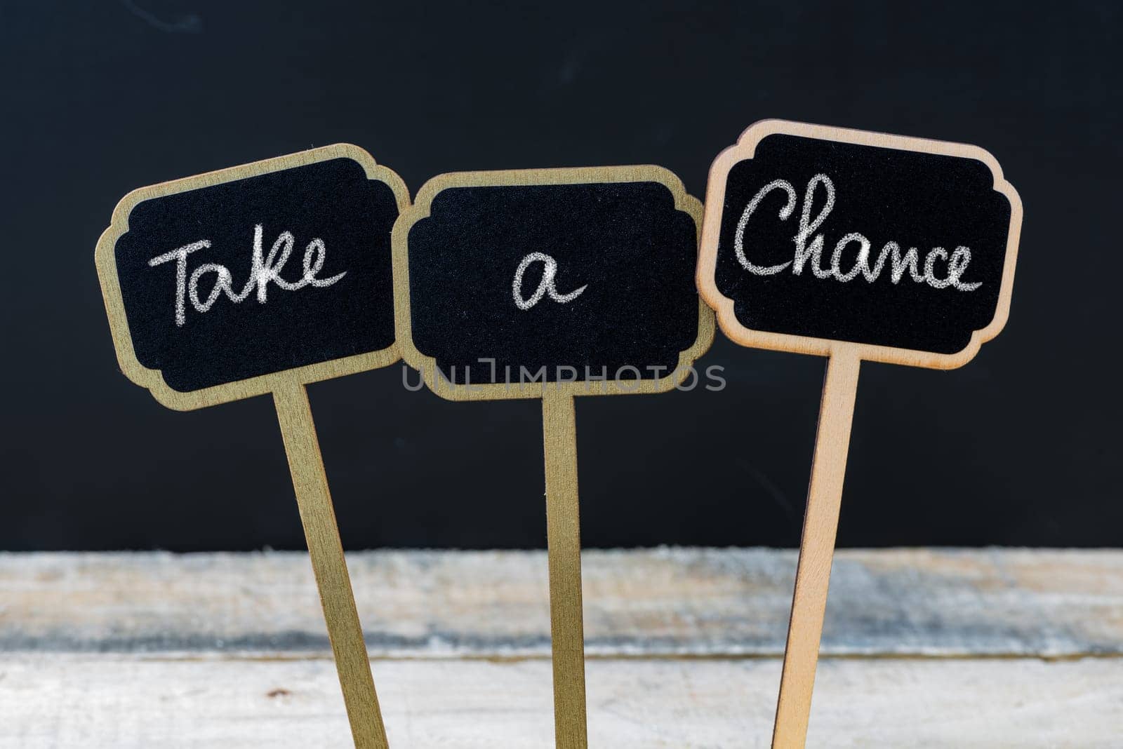 Motivational message Take A Chance written with chalk on wooden mini blackboard labels, defocused chalkboard and wood table in background