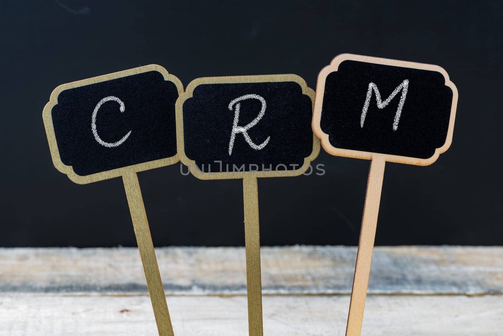 Business message CRM Customer Relationship Management written with chalk on wooden mini blackboard labels, defocused chalkboard and wood table in background