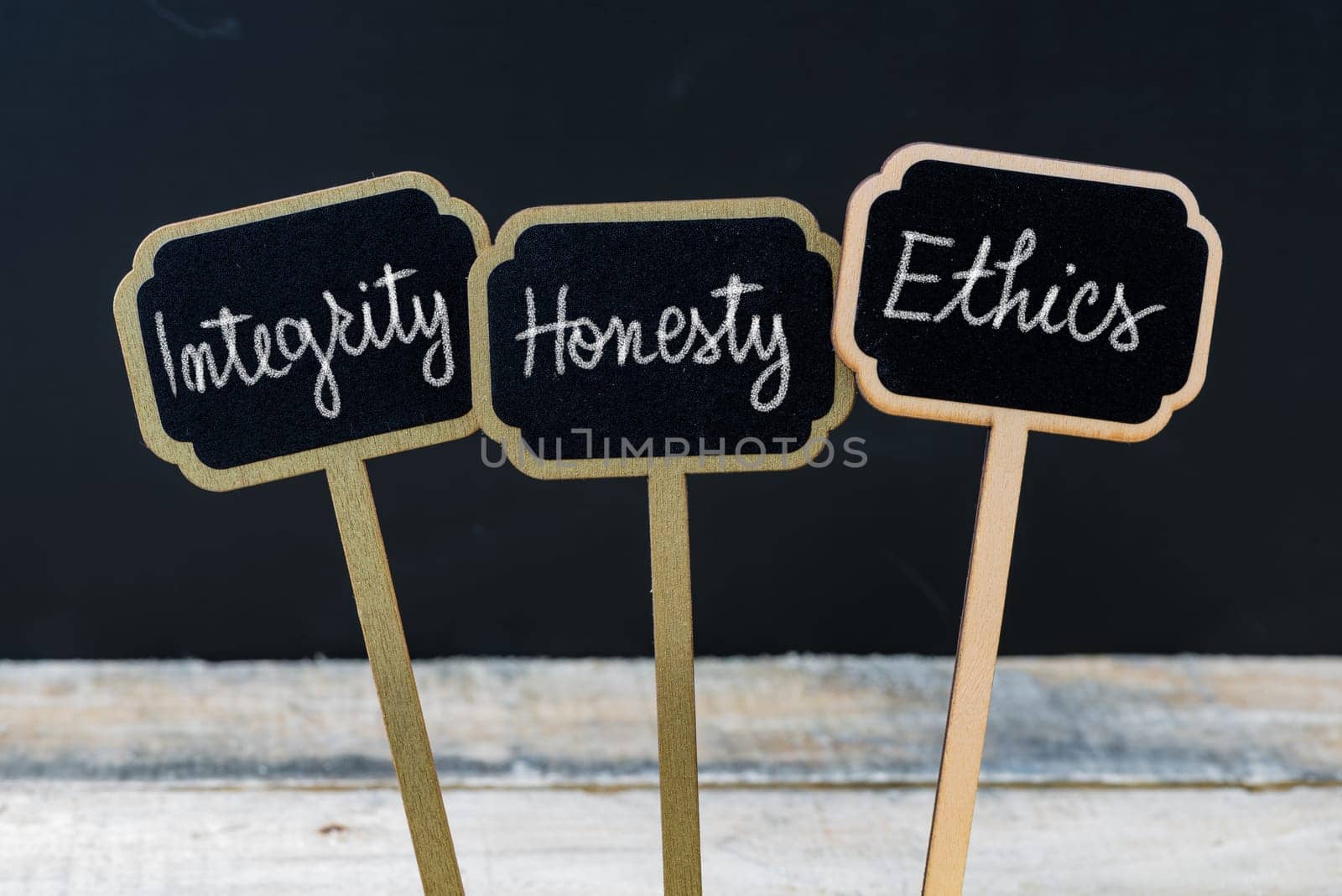 Business message Integrity, Honesty, Ethics written with chalk on wooden mini blackboard labels, defocused chalkboard and wood table in background