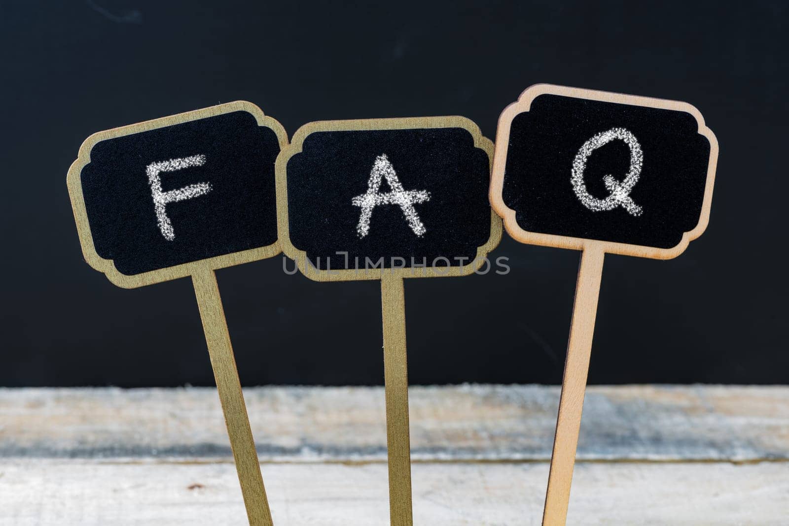 Business message FAQ as Frequently Asked Questions written with chalk on wooden mini blackboard labels, defocused chalkboard and wood table in background