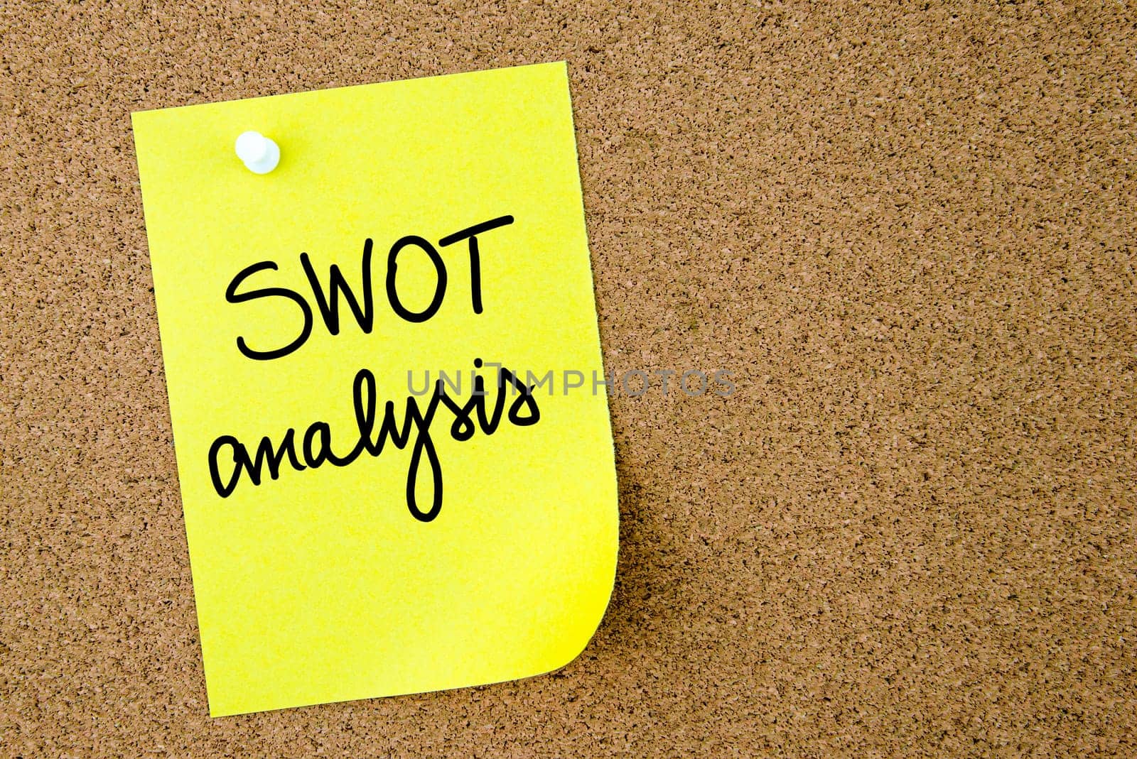 SWOT Analysis text written on yellow paper note pinned on cork board with white thumbtack. Business concept image with copy space available