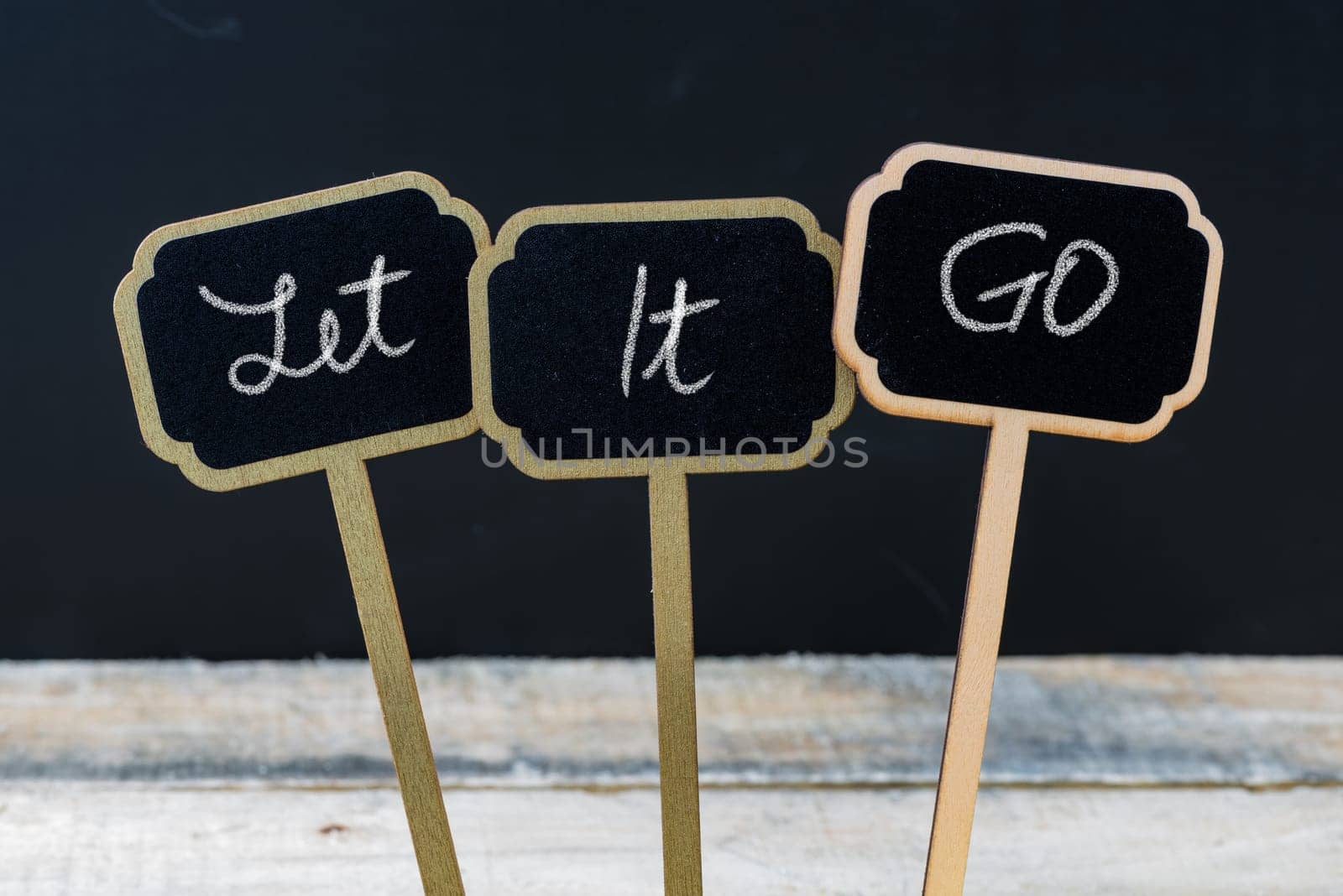 Business message Let It GO written with chalk on wooden mini blackboard labels, defocused chalkboard and wood table in background