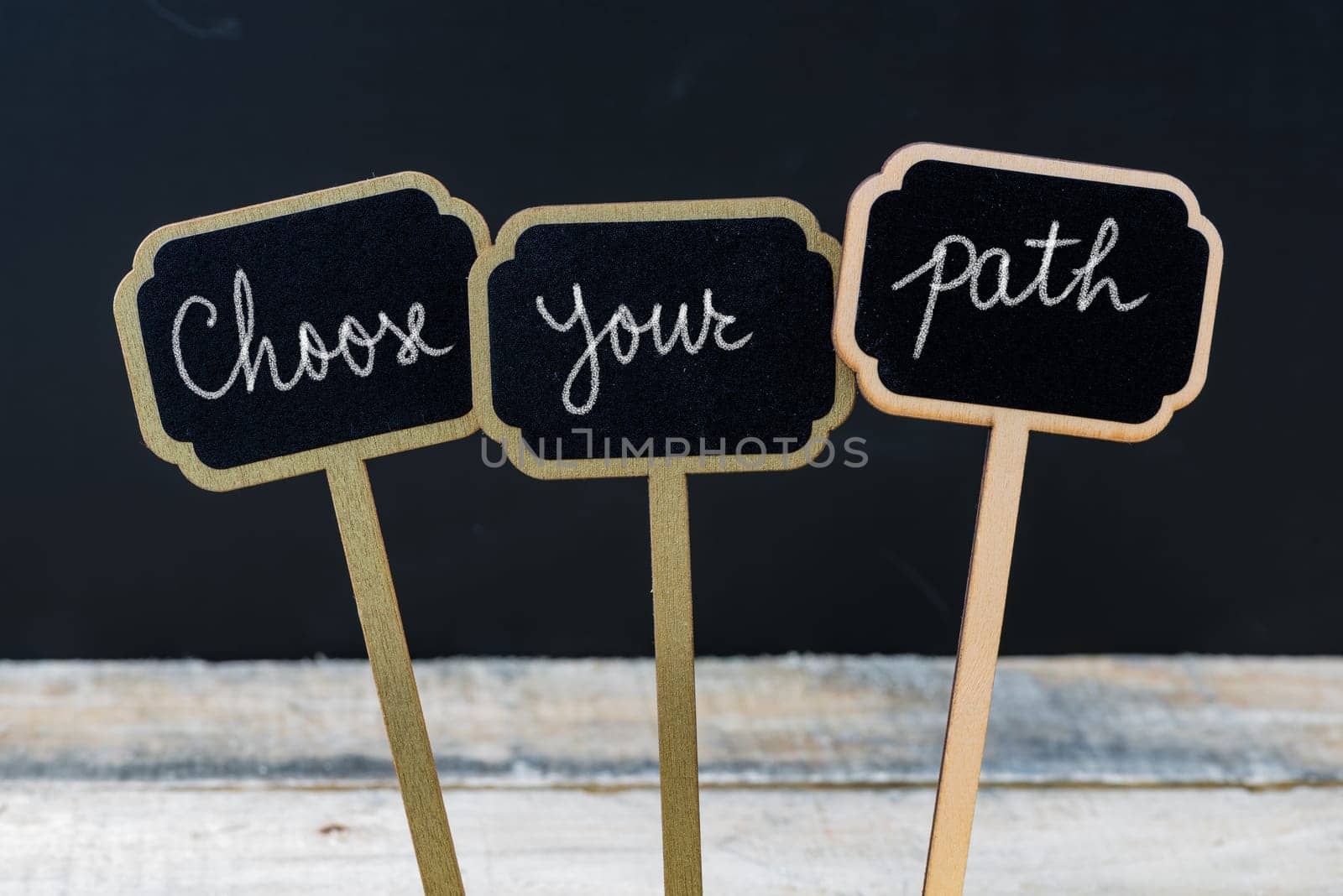Motivational message Choose Your Path written with chalk on wooden mini blackboard labels, defocused chalkboard and wood table in background