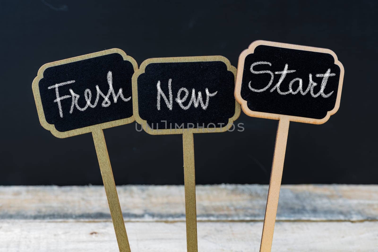 Business message Fresh New Start written with chalk on wooden mini blackboard labels, defocused chalkboard and wood table in background